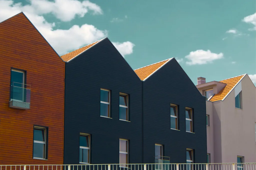 Moderne huizen met donkere en houten gevelbekleding en oranje dakpannen onder een blauwe lucht met wolken.