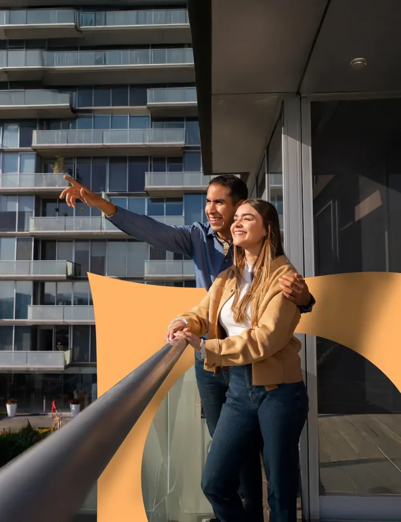 Een lachend stel staat op het balkon van een modern appartementencomplex en kijkt samen in de verte.