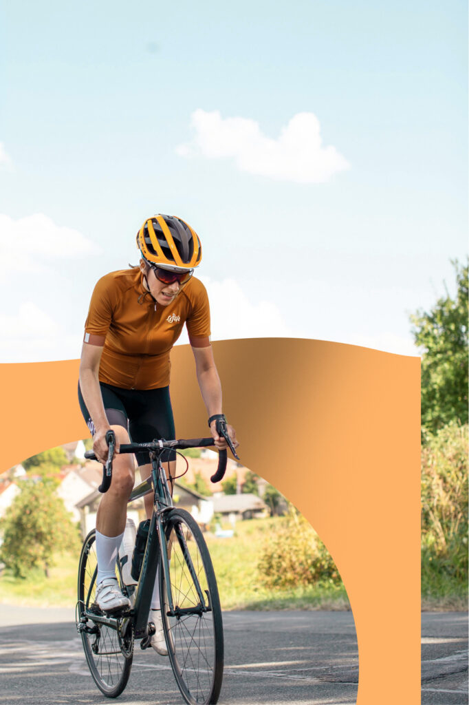 Wielrenner in oranje tenue en bijpassende helm fietst op een landelijke weg.