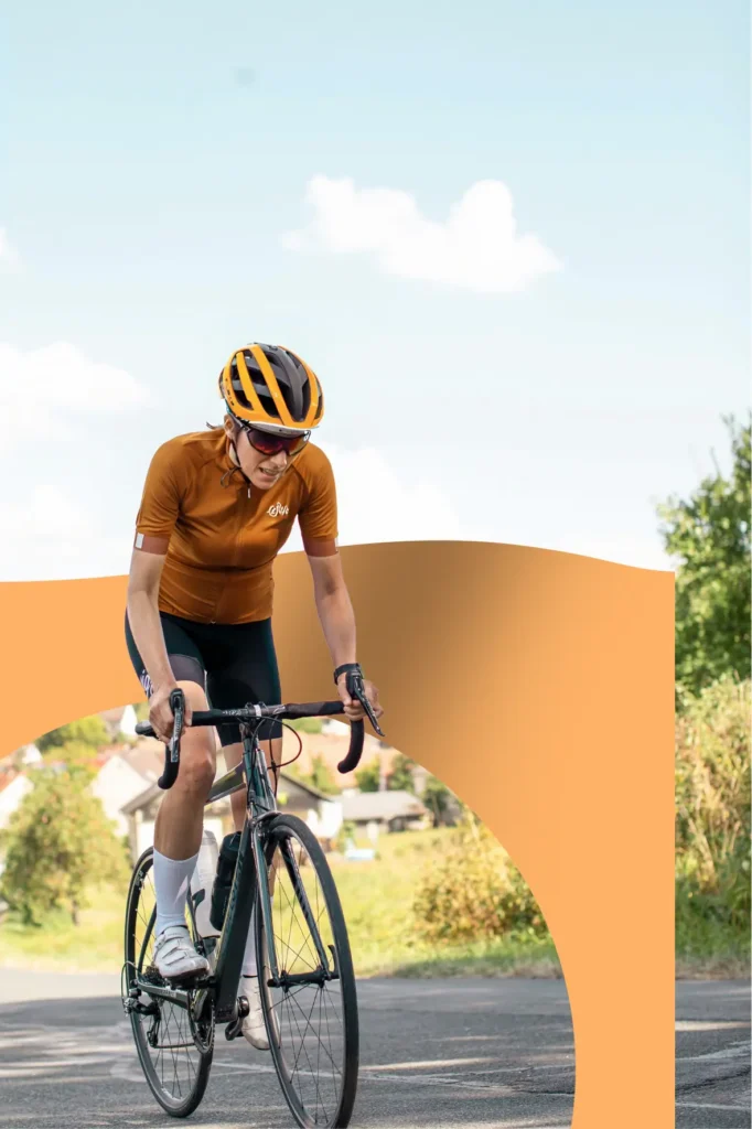 Wielrenner in oranje tenue en helm fietst op een zonnige dag over een landelijke weg.